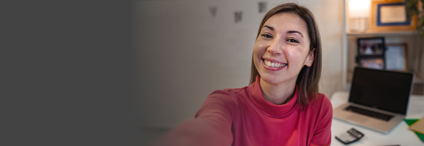 A smiling student sitting at her desk at home taking a selfie