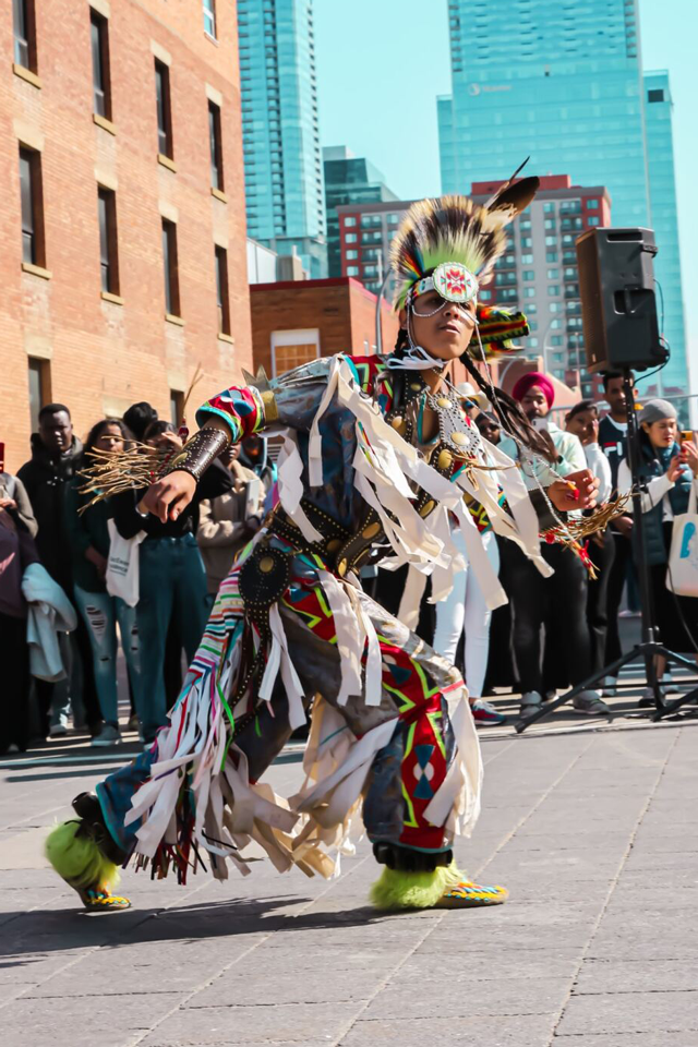 An Indigenous dancer performing in front of a crowd wearing traditional regalia