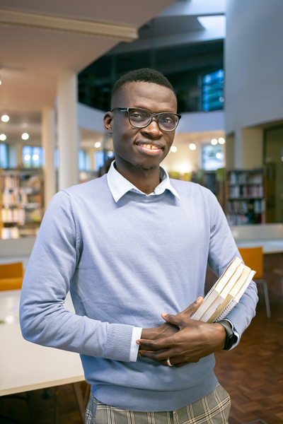 A male college student in a library holding a stack of books