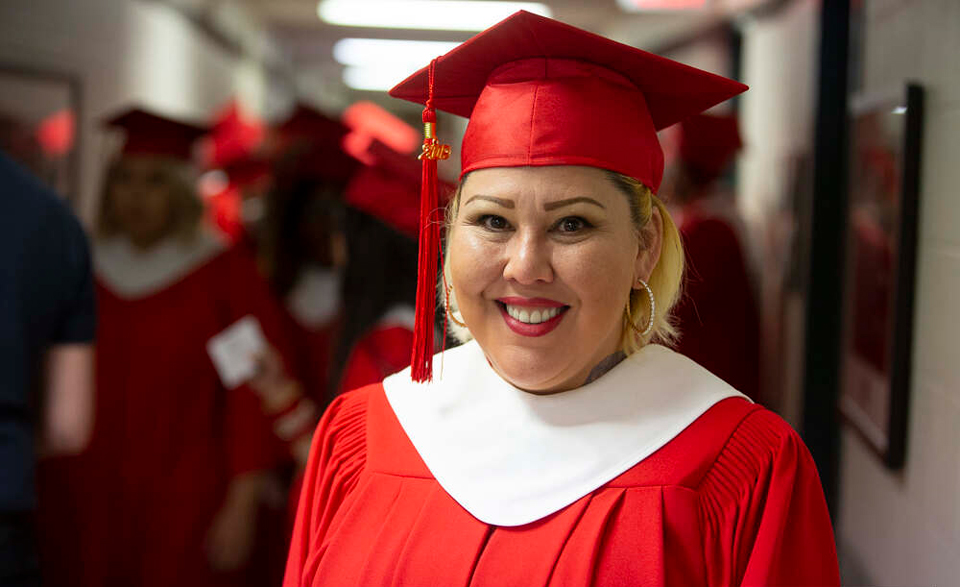 An Indigenous women wearing a red graduation cap and gown.