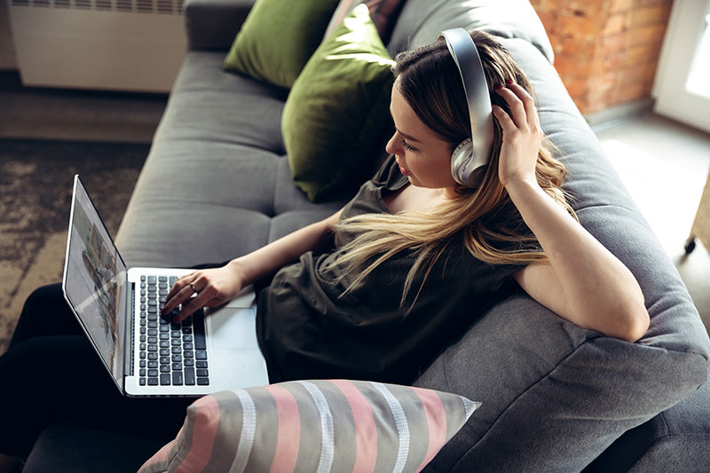 A women sitting on a couch wearing headphones with a laptop in her lap