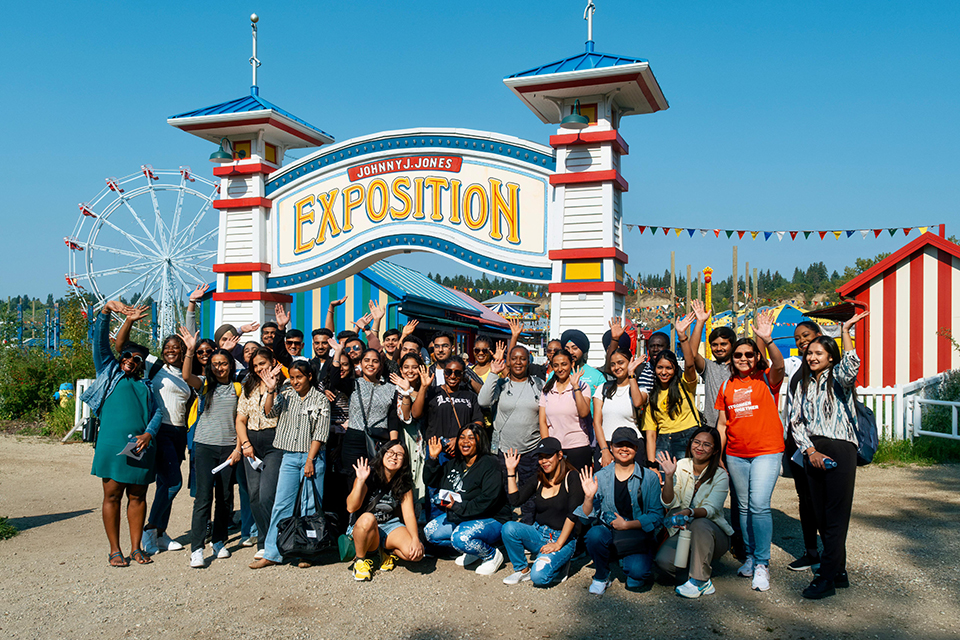 A large group of international students posing in front of a sign at Fort Edmonton Park